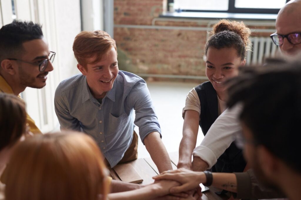 A diverse group of young professionals joining hands in a cheerful and supportive team-building activity.